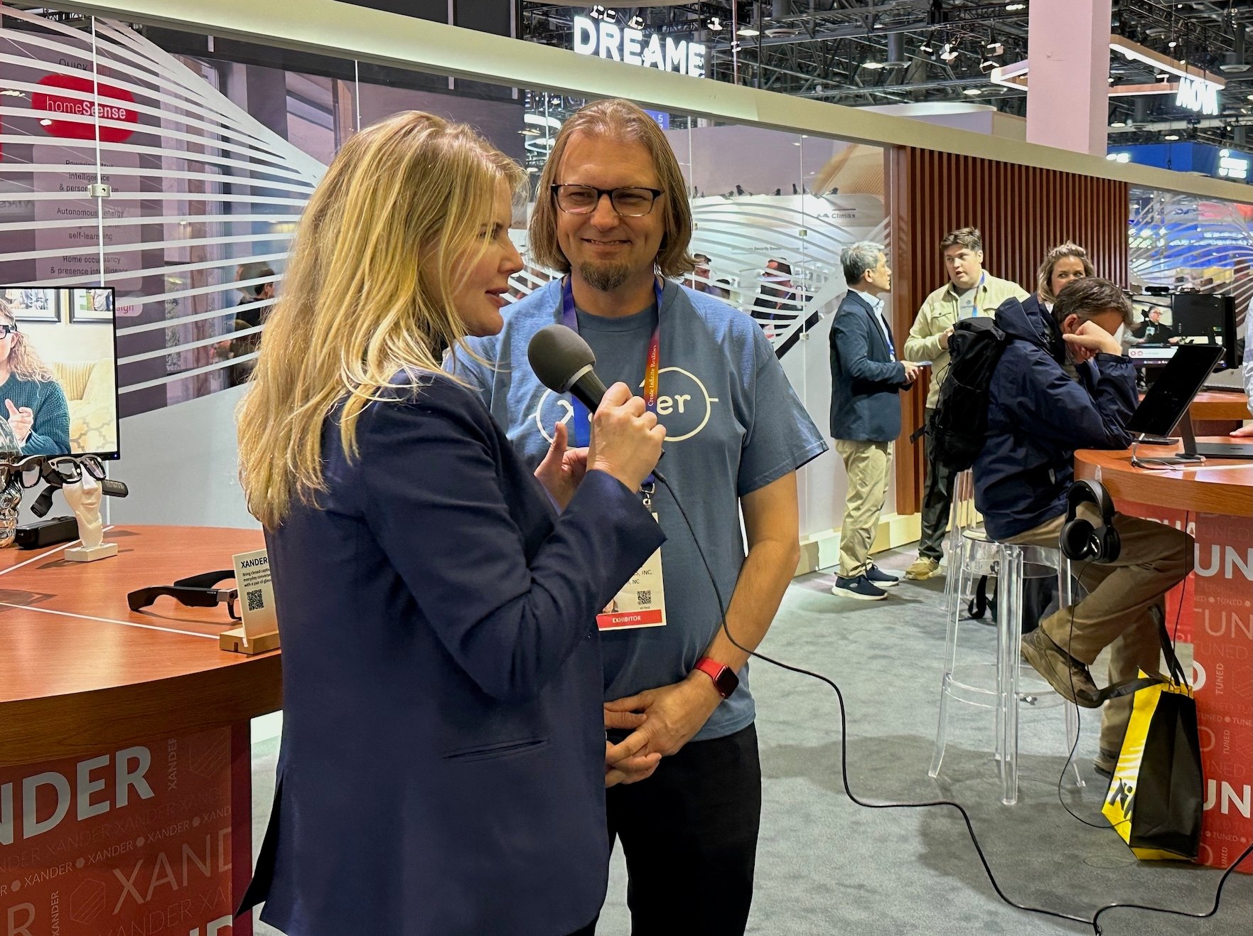 Woman reporter interviewing man wearing glasses at trade show, with crowd in backround 
